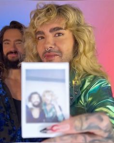 a man with long hair and piercings holding up a photo in front of him