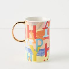 a coffee cup with the words happy written on it in different colors and shapes, sitting on a white surface