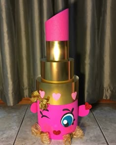 a pink and gold birthday cake with hearts on it's face, sitting on a tile floor