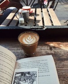 an open book sitting on top of a wooden table next to a cup of coffee