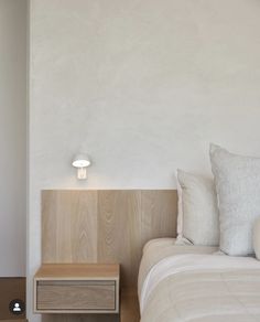 a bed with white sheets and pillows next to a wooden night stand on the floor