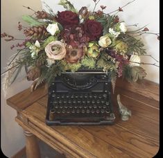 an old fashioned typewriter with flowers and greenery on it sitting on a table