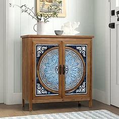 a wooden cabinet with blue and white designs on the front door, next to a potted plant