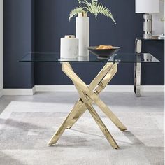 a glass table with gold metal legs and a plant on top in front of a blue wall