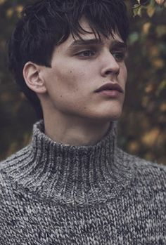 a young man with dark hair wearing a turtle neck sweater and looking off into the distance