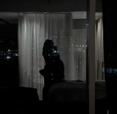 a woman standing in front of a window next to a night time scene with the lights on