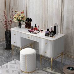 a white vanity with gold accents and flowers in vases next to it on a marble floor