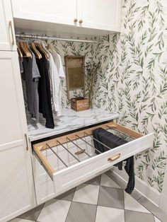 an open drawer in a closet with clothes hanging on the wall and green leaves on the wall