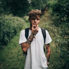 a young man with tattoos on his arm is standing in the woods