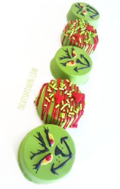 three decorated cookies sitting on top of a white table next to each other with green frosting and red sprinkles