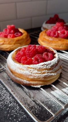 raspberries on top of powdered sugar covered pastries sitting on a cooling rack