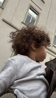 a small child with curly hair sitting on the back of a woman's shoulder