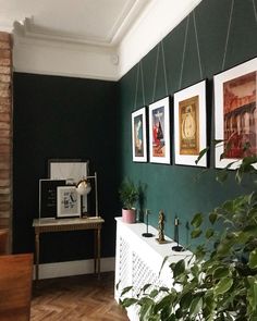 a living room with green walls and pictures on the wall, plants in vases