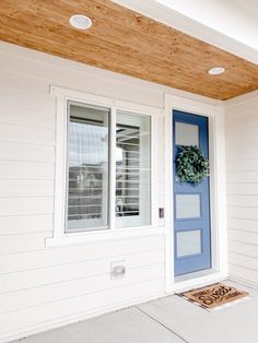 a blue front door on a white house with a wooden ceiling and wood paneling