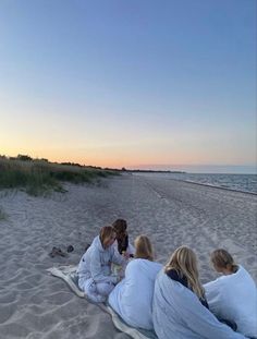 three women sitting on the beach with blankets wrapped around their backs and one woman holding a cell phone