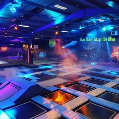 an indoor trampoline area with blue lights and fire in the air, surrounded by floor mats