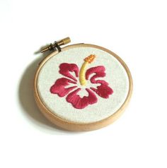 a red and yellow flower embroidered on a white surface with a wooden hoop hanging from it