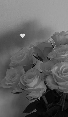 a vase filled with white roses and a small heart on the wall behind it in black and white