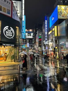 people are walking down the street in the city at night with umbrellas and neon signs