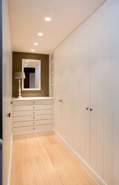 an empty room with wooden floors and white cabinets on the wall, in front of a large mirror