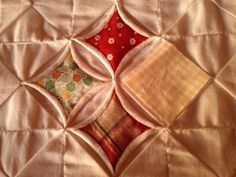 a close up of a quilt on a bed with white sheets and red pillow cases