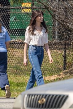 two women walking down the street in front of a fenced area with cars behind them