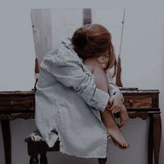 a woman sitting in front of a mirror on top of a wooden table next to a stool