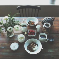 a wooden table topped with white bowls filled with food and cups on top of it