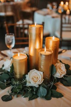 some candles are sitting on a table with white flowers and greenery around the edges