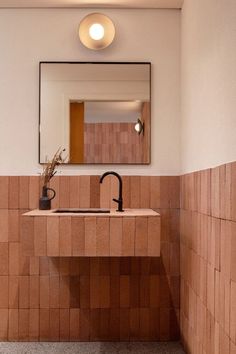 a bathroom sink sitting under a mirror next to a wall mounted faucet with a vase on it