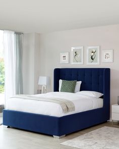 a bed with blue headboard and foot board in a white walled room next to a window