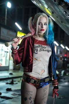 a woman with blue hair and makeup holding a baseball bat in her hand while standing on the street