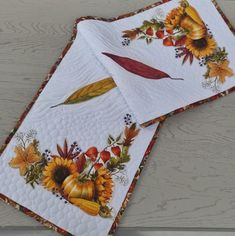 two quilted placemats decorated with autumn leaves and sunflowers