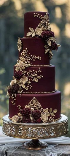 a three tiered cake with red frosting and gold flowers on it's side