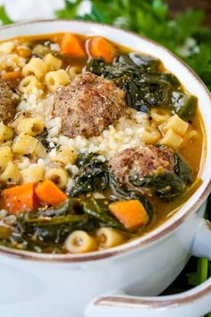 a white bowl filled with meatballs and pasta soup on top of a wooden table