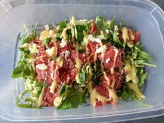 a plastic container filled with salad covered in cheese and dressing on top of lettuce