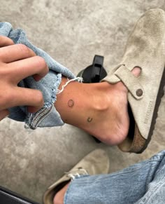 a person with a small tattoo on their left foot, sitting down and holding onto a pair of jeans