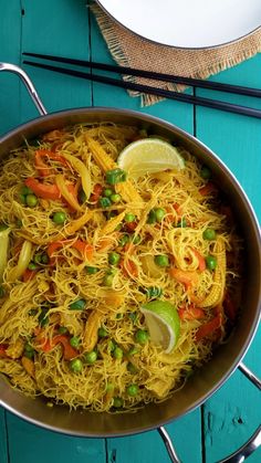 a pan filled with noodles and vegetables on top of a blue wooden table next to a plate