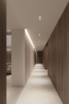 a long hallway with white walls and wood paneling on both sides is lit by recessed lighting