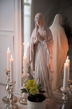 a statue and candles on a table in front of a mirror with the image of mary