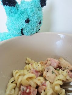 a fork in a bowl with pasta and meat on it next to a stuffed animal