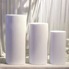 three white vases sitting next to each other on a counter top in front of a window