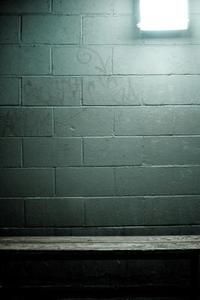 a person sitting on a bench in front of a brick wall with a light coming through the window