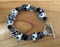 This is an interesting black and white glass bracelet that would look great with almost any outfit you choose to wear. Some of the beads have a raised patterns and there are four granulated silver beads and it has a silver toggle closure. This black and white furnace glass bracelet has some unusual beads on it, and you will enjoy picking it up often to wear. The  black and white bracelet makes a stunning statement 8 inches long White Adjustable Bracelets With Toggle Clasp, Adjustable White Bracelets With Toggle Clasp, Black Handmade Novelty Beaded Bracelets, Handmade Black Glass Jewelry, Black Glass Jewelry With Polished Beads, Glass Multi-strand Jewelry With Large Beads, Vintage Black Glass Jewelry, White Bracelets, Glass Bracelet