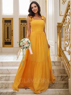 a woman in a long yellow dress standing on steps with flowers and holding a bouquet