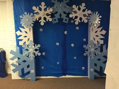 a blue and white backdrop with snowflakes hanging from it's sides in front of a brick wall