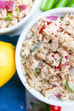 two white bowls filled with tuna salad next to lemons and celery sticks