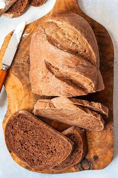 a wooden cutting board topped with loaves of bread next to a loaf of bread