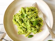 a white plate topped with pasta covered in pesto sauce and garnished with green leaves