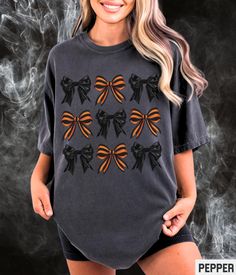 Our Comfort Colors Halloween retro style graphic tee features coquette orange striped and black bows. Our crewneck pairs perfectly with other matching style variations (linked below). ✩ ✩ 𝗔𝗱𝘂𝗹𝘁 𝗖𝗼𝗺𝗳𝗼𝗿𝘁 𝗖𝗼𝗹𝗼𝗿𝘀 𝗧𝗲𝗲: https://starrieapparel.etsy.com/listing/1760615242 ✩ 𝗔𝗱𝘂𝗹𝘁 𝗚𝗶𝗹𝗱𝗮𝗻 𝗦𝘄𝗲𝗮𝘁𝘀𝗵𝗶𝗿𝘁: Halloween Coquette Bows Shirt, Girly Halloween Tshirt, Preppy Cottagecore Graphic Tee Spooky Girl Aesthetic Comfort Colors Plus Size T-shirt SIZE UP for an OVERSIZED FIT (see size chart in listing photos). ✩ Our shop uses direct-to-garment printing to make our products. The design ink is sprayed on, then allowed to soak into the fibers of the garment. This process yields fine quality prints and a smooth finish on the garment. 𝗖𝗢𝗠𝗙𝗢𝗥𝗧 𝗖𝗢𝗟𝗢𝗥𝗦® Garment Retro Black T-shirt For Fall, Black Retro T-shirt For Fall, Spooky Girl Aesthetic, Preppy Cottagecore, Halloween Coquette, Girly Halloween, Black Bows, Coquette Bows, Halloween Retro